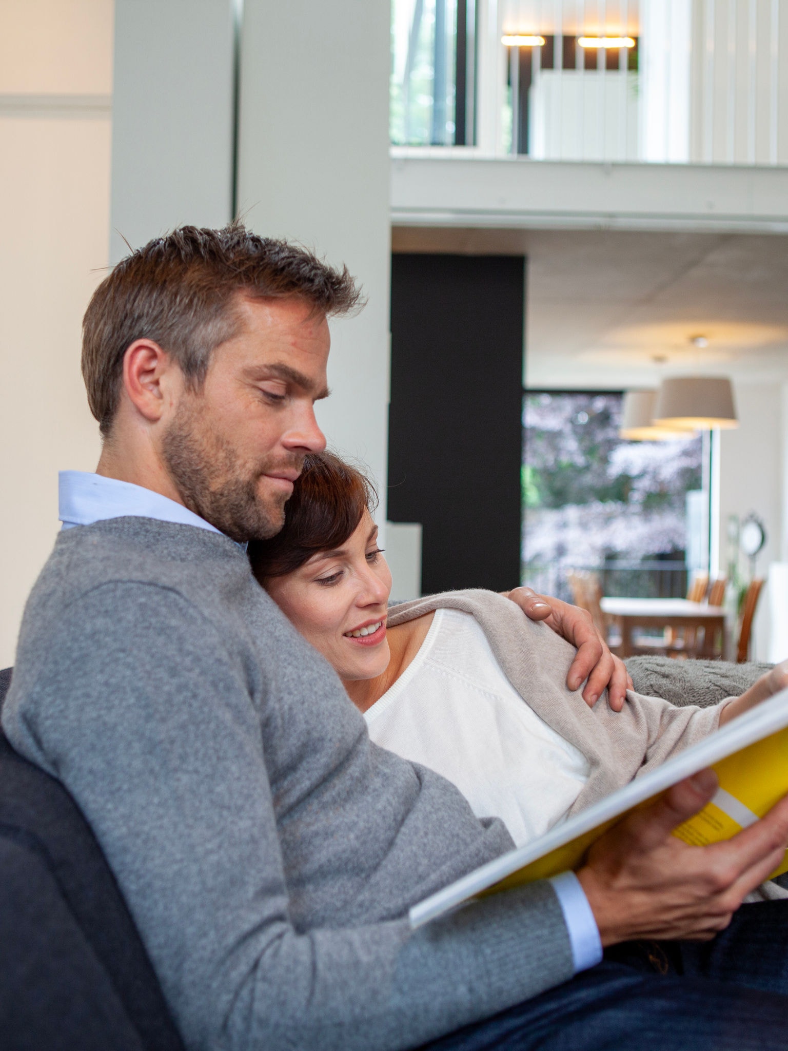 Casal abraçado a relaxar no sofá e a ler um livro à temperatura perfeita