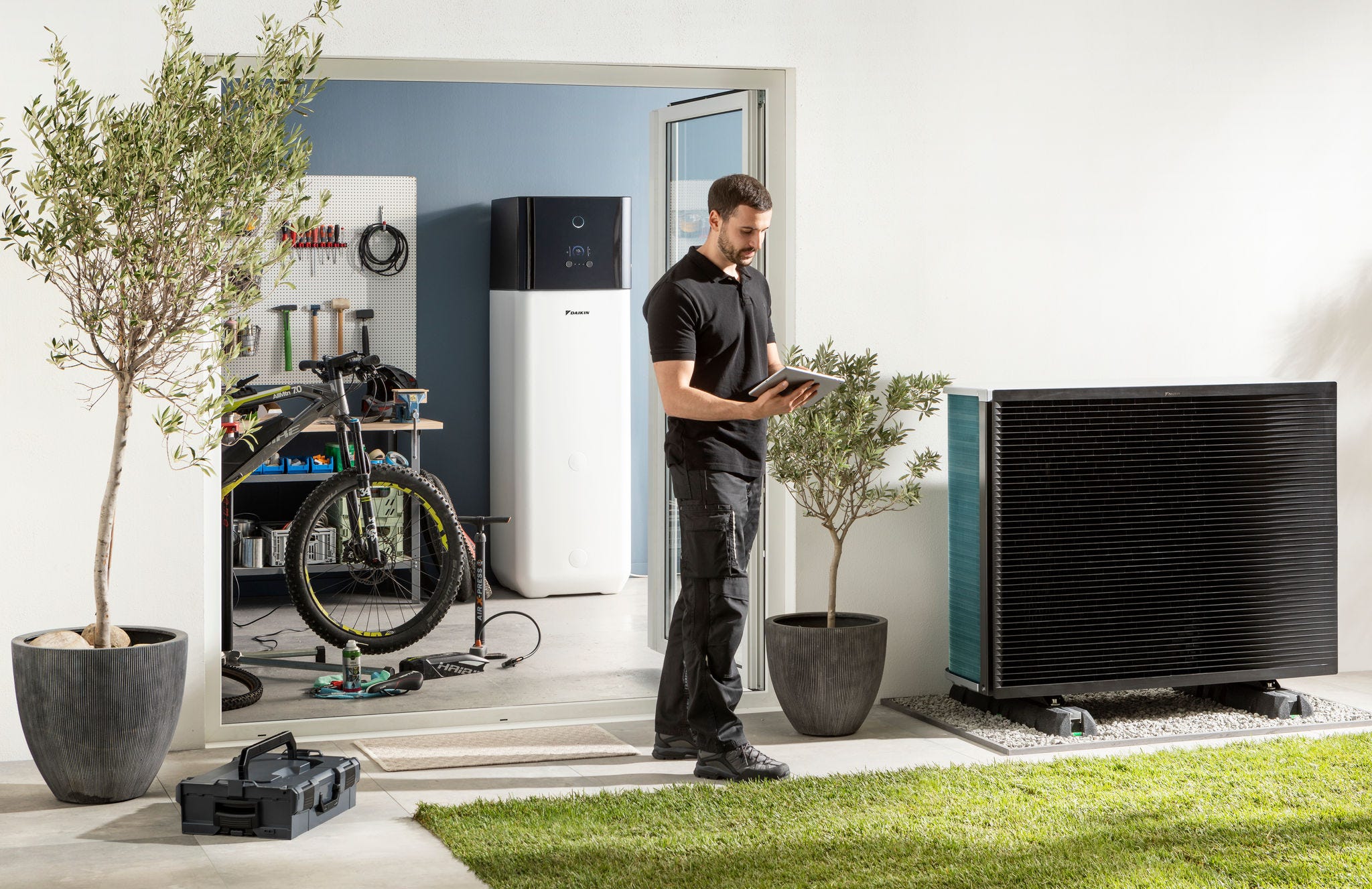Instalador a verificar a unidade exterior da bomba de calor aerotérmica e o depósito de água quente