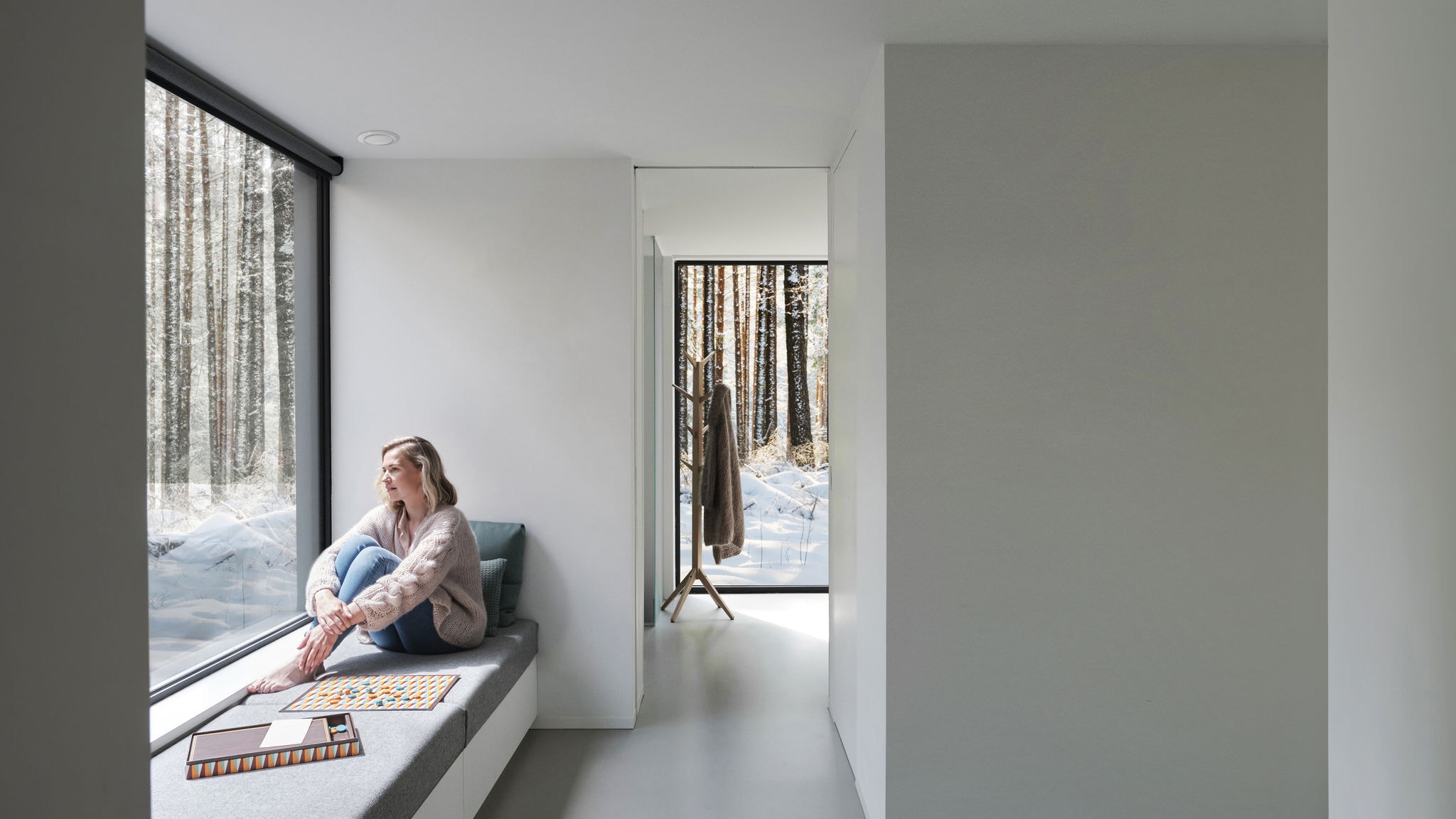 Grande plano de uma mulher sentada à frente de uma janela, descalça, a olhar para as árvores e para a neve.