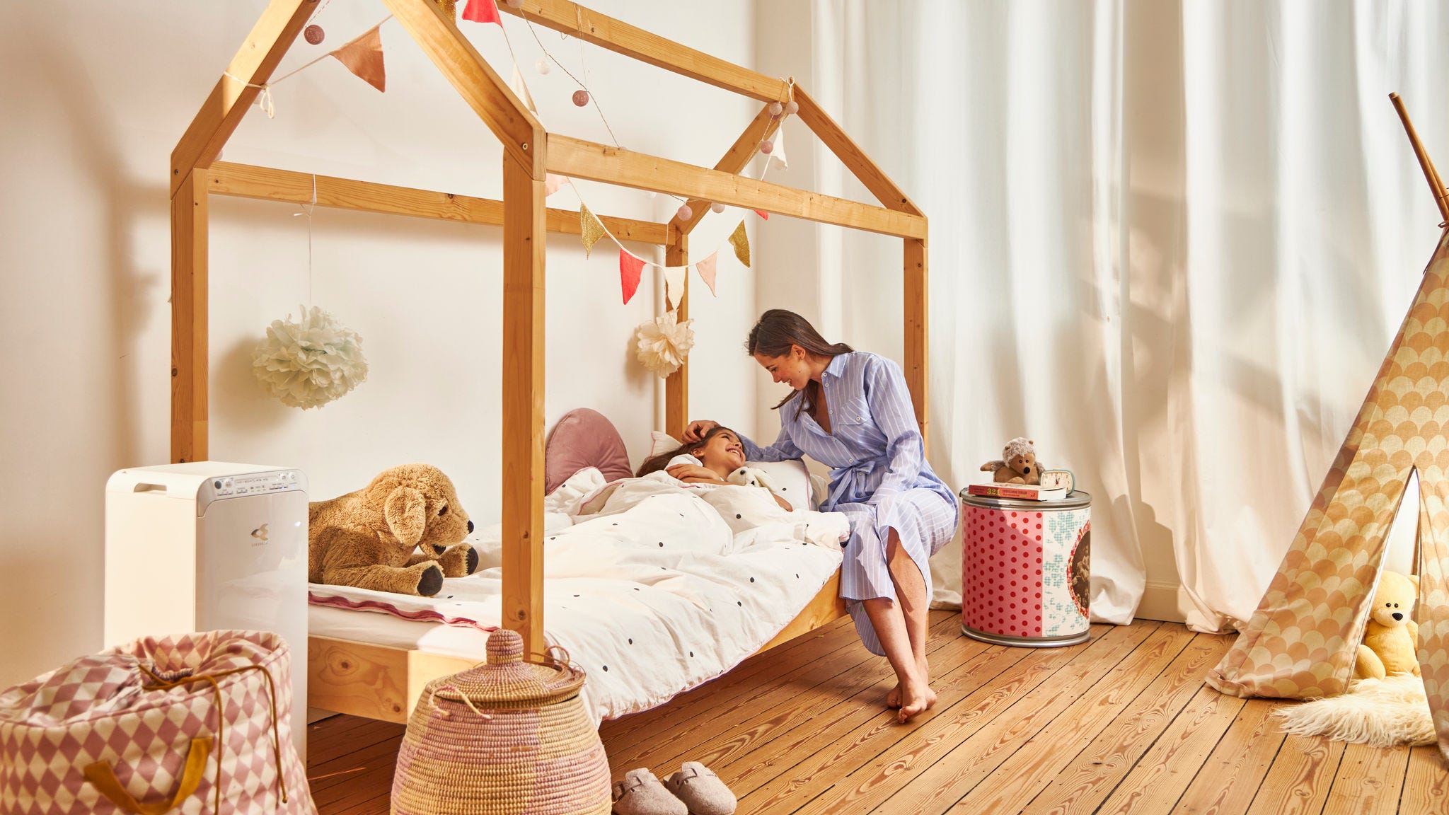 Mãe a colocar criança na cama na sua habitação saudável graças ao purificador de ar Daikin no quarto das crianças