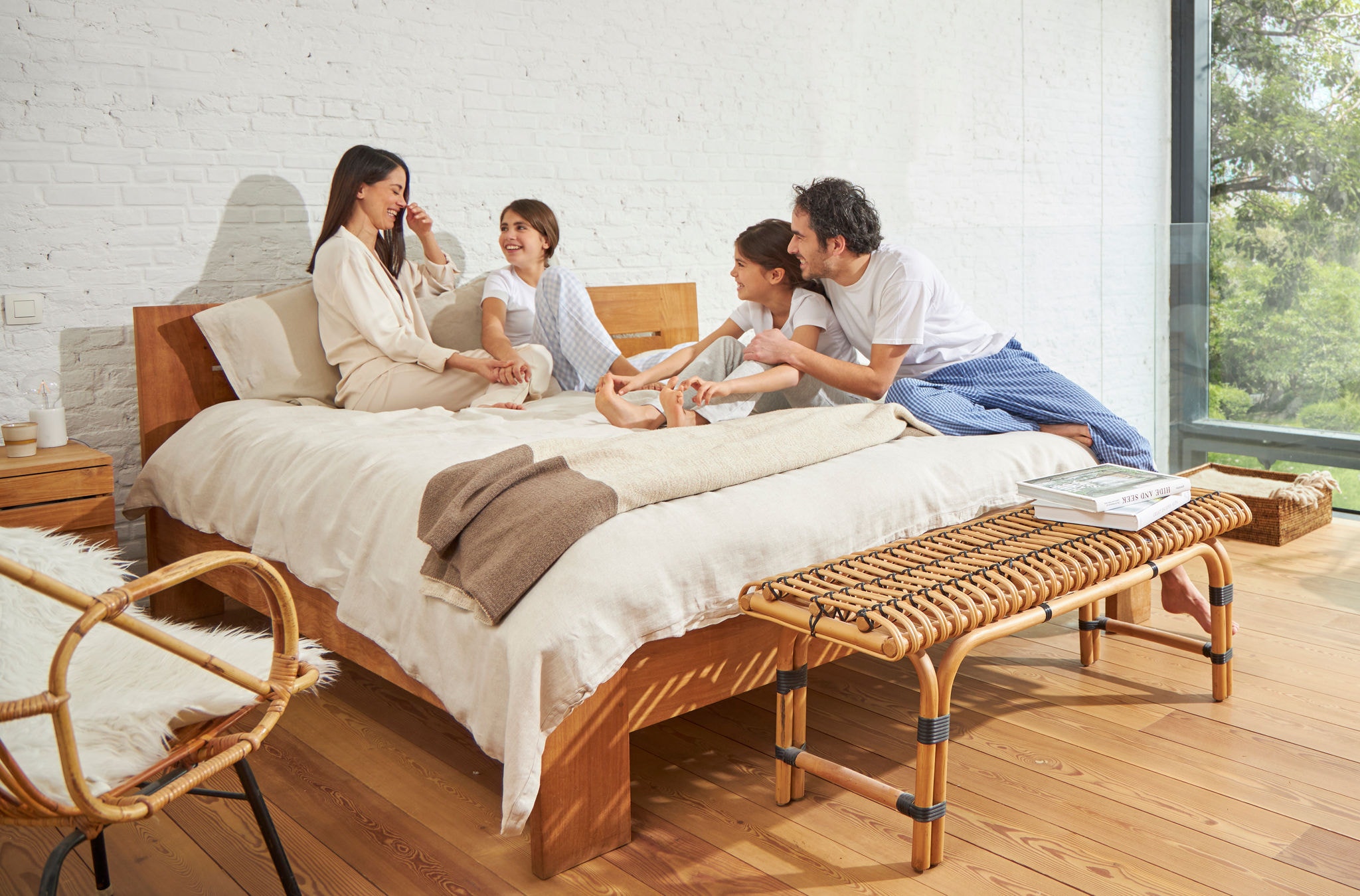 Uma mulher e um homem sentados numa cama com duas meninas, relaxados, a rirem-se e a desfrutarem de ar saudável.