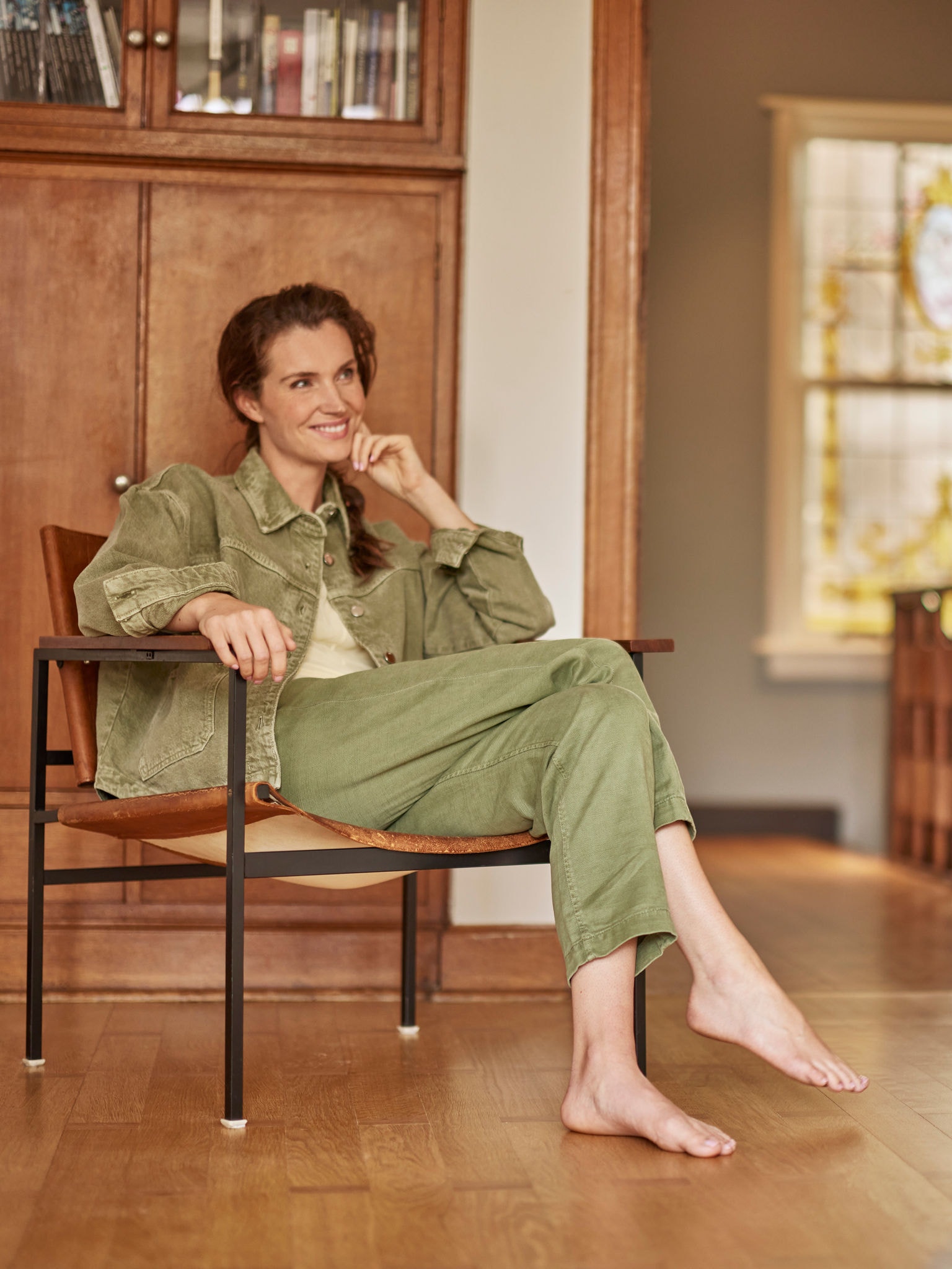 Mulher sentada numa poltrona, descalça, sorridente a olhar para a frente.