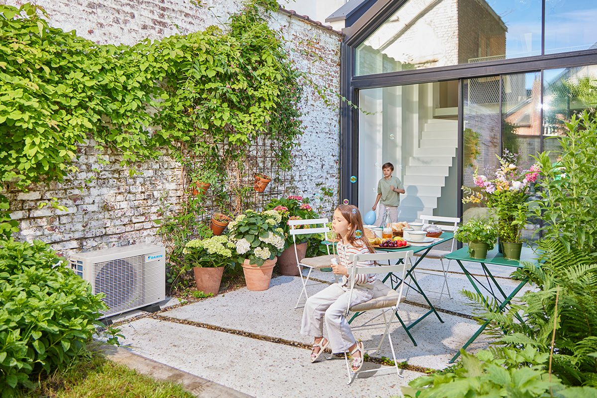 Crianças a brincar com berlindes num terraço ajardinado ao lado de uma bomba de calor exterior